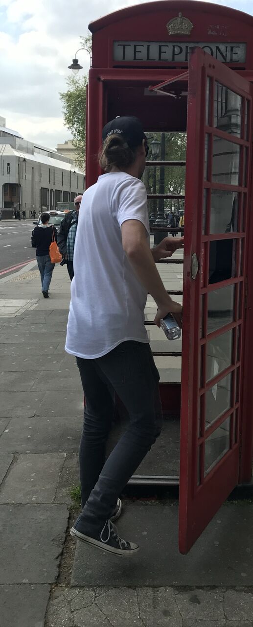 Someone stepping into a red phone box on a London pavement, door held open.
