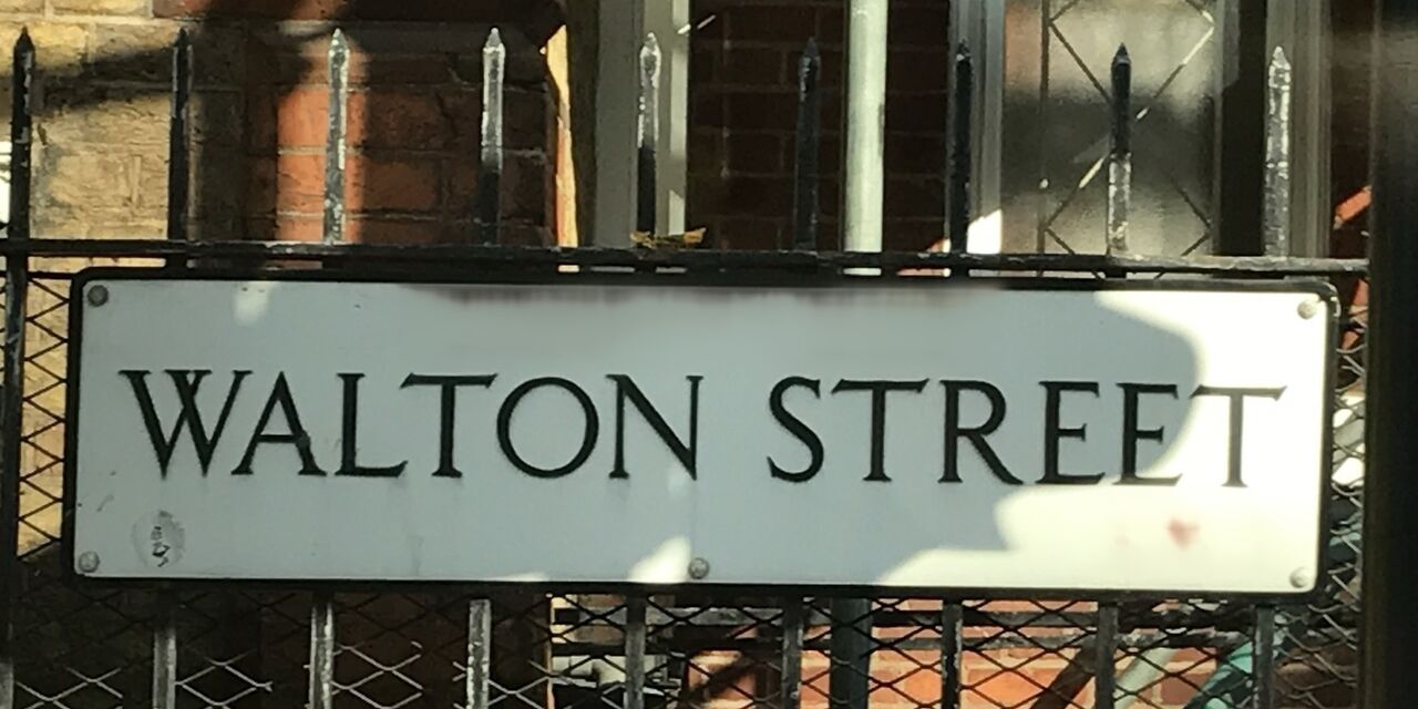 A white enamel street sign on black railings: WALTON STREET.