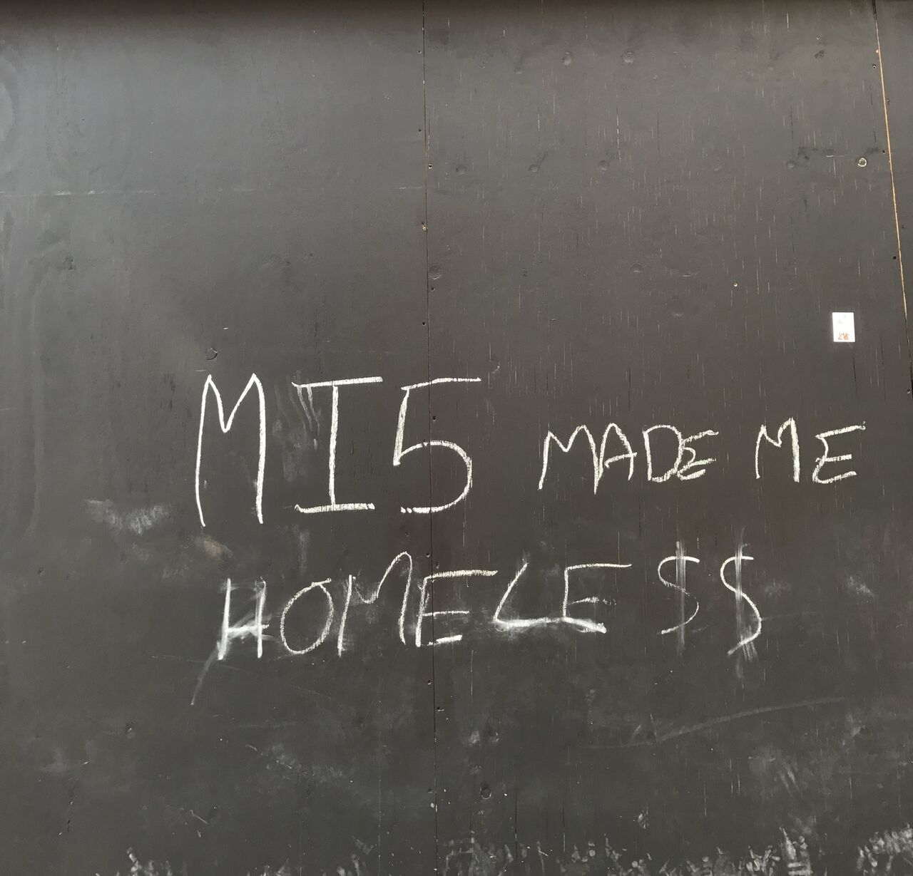 Chalk on black hoarding: MI5 MADE ME HOMELESS.
